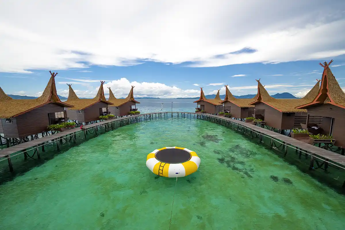 Have fun on the water trampoline in our lagoon. Symmetrical view of Dayang Resort's overwater chalets with their distinctive high-peaked roofs, surrounding a water trampoline in a clear turquoise lagoon.